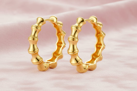 Close-up of gold-plated sterling silver hoop earrings with bamboo-inspired segmented design on white background.