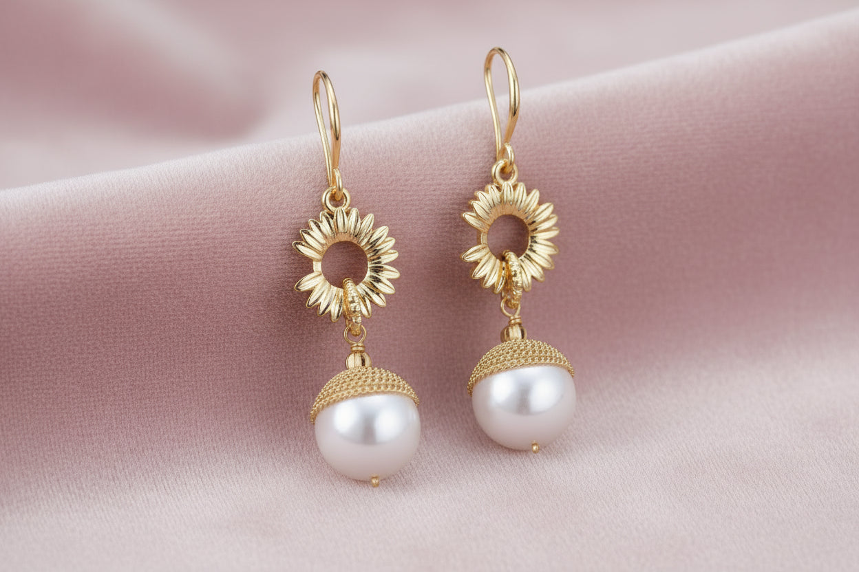 Gold sunburst charm earrings with baroque pearl drops on French hooks against cream background