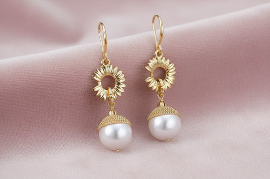 Gold sunburst charm earrings with baroque pearl drops on French hooks against cream background