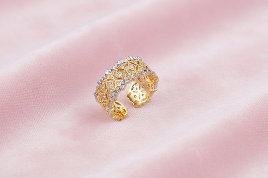 Two-tone ring with geometric lattice pattern in gold and silver finish with crystal accents on beige background