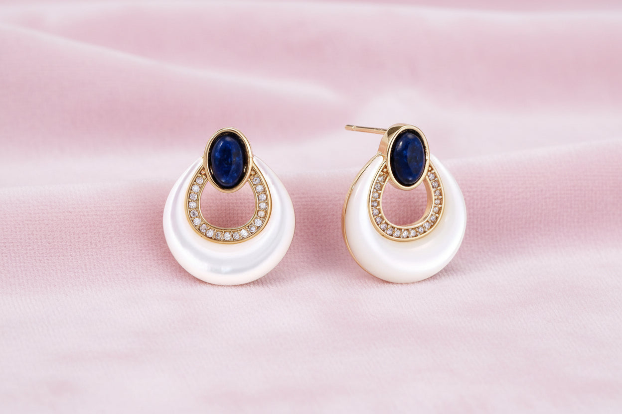 Gold drop earrings with oval lapis lazuli, crystal-paved frame, and iridescent mother-of-pearl teardrop on cream background