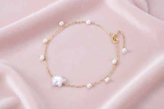 Delicate gold chain bracelet with baroque pearl centerpiece and small freshwater pearls on cream background.