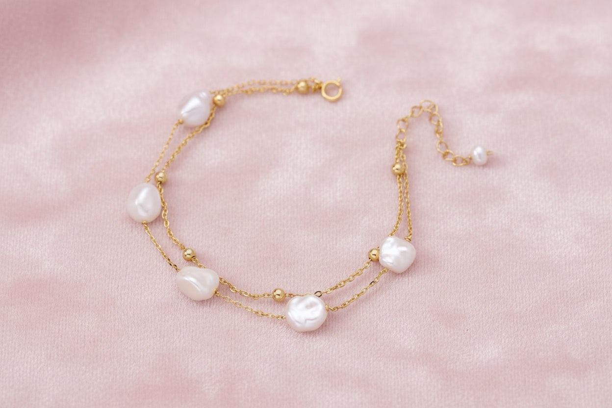 Double-strand gold bracelet with irregular baroque pearls and smooth freshwater pearls on cream background.