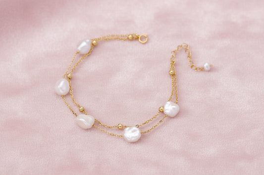 Double-strand gold bracelet with irregular baroque pearls and smooth freshwater pearls on cream background.