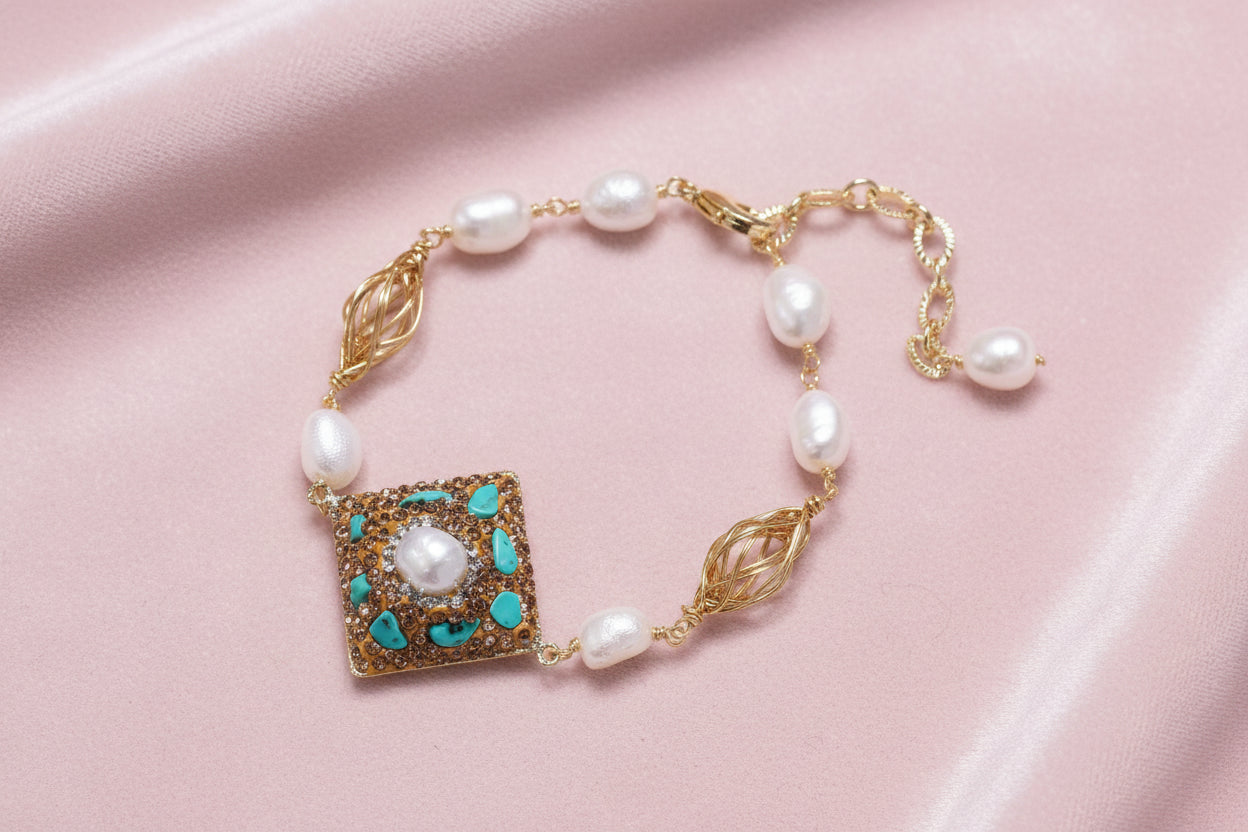 Gold-plated bracelet with baroque centerpiece, turquoise stones, freshwater pearls, and ornate chain links on cream background.