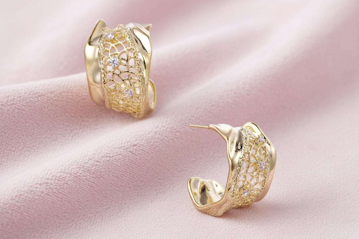 Gold-plated sculptural hoop earrings with geometric lattice centerband and sparkling zirconia on white background.