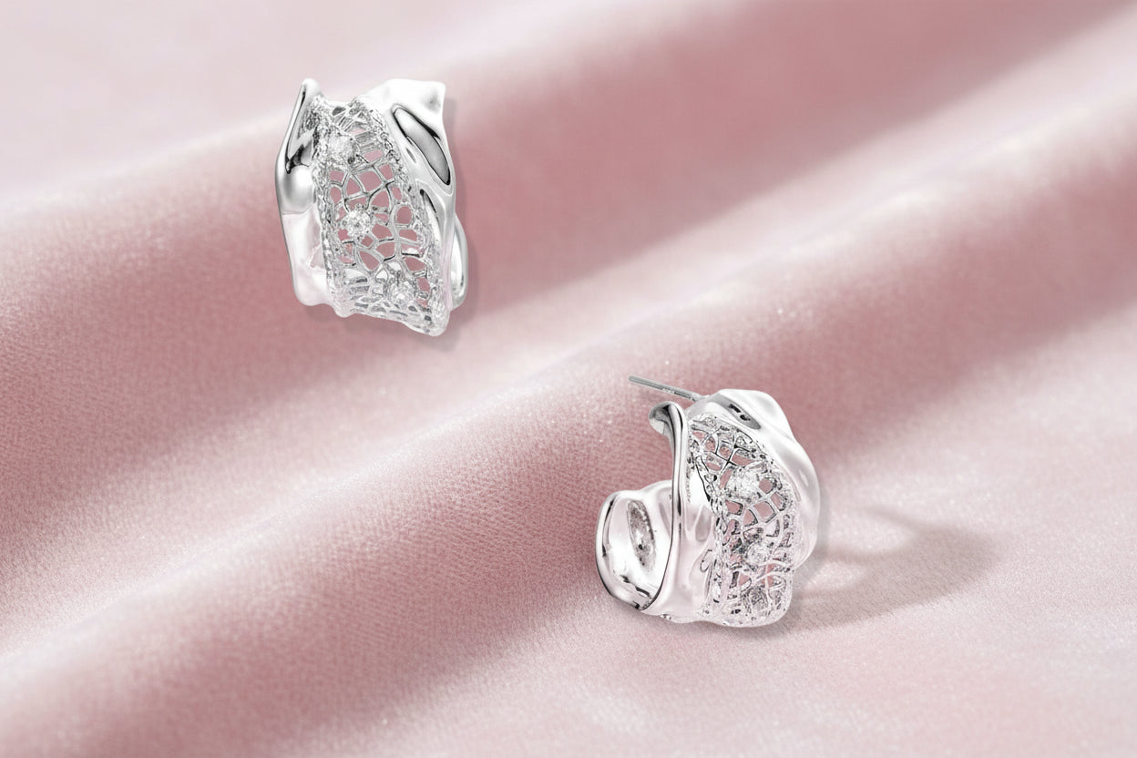 Close-up of sculptural hoop earrings with lattice center band and smooth twisted edges in white gold-plated brass with zirconia