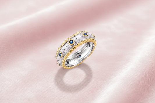 Two-tone ring with brushed silver center, gold beaded edges, and blue zirconia stones on white background.
