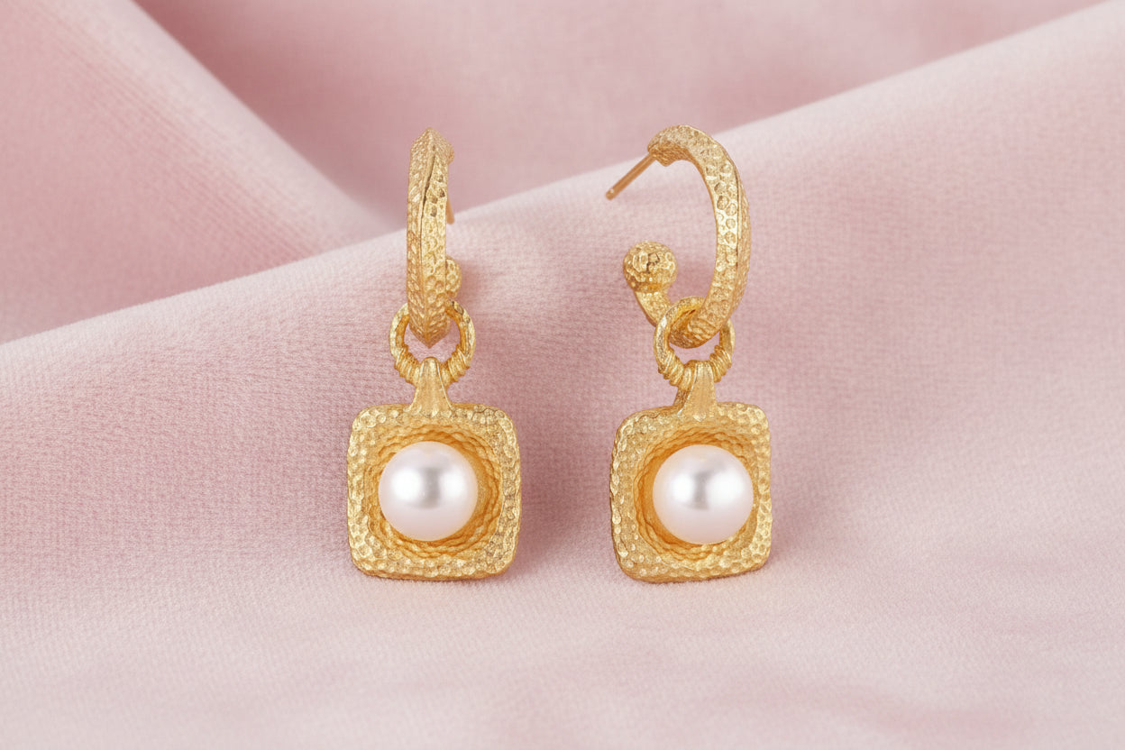 Pair of gold vermeil hoop earrings with textured square frames holding freshwater pearls on cream background