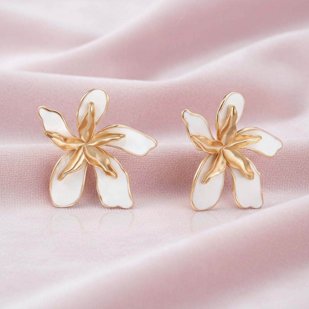 White enamel tropical flower earrings with sculptural gold-plated center and organic petal design on cream background