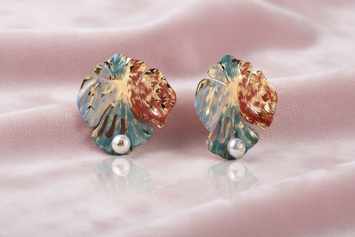 Artistic monstera-shaped earrings with teal, coral, and cream enamel brushstrokes, gold trim, and white pearl accent