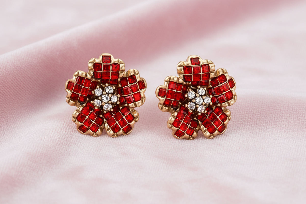 Gold-plated flower studs with burgundy square crystals in petal mosaic and clear center stones on beige background.