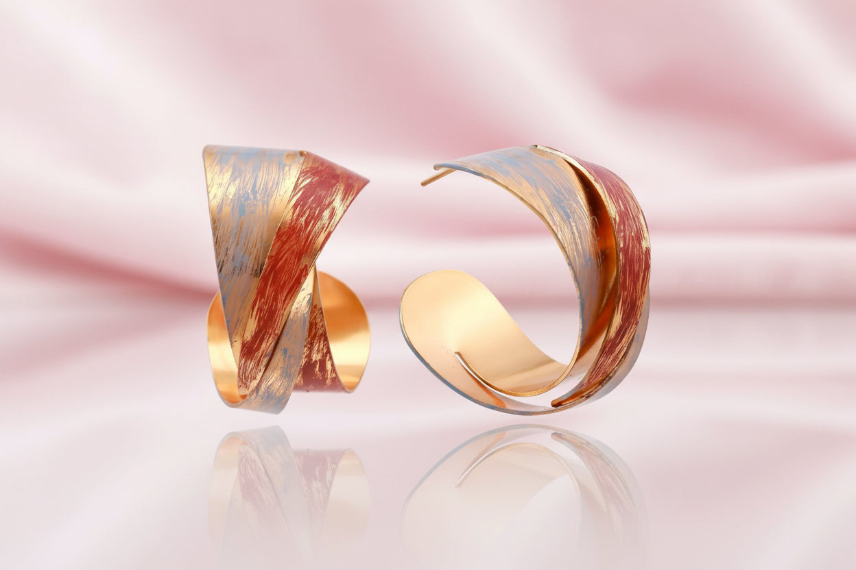 Sculptural gold-plated hoop earrings with diagonal purple and coral enamel stripes in twisted ribbon design