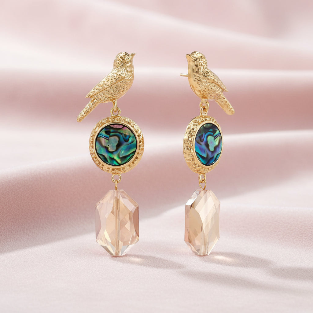 Gold-plated bird stud earrings with iridescent abalone shell medallions and champagne crystal drops on cream background