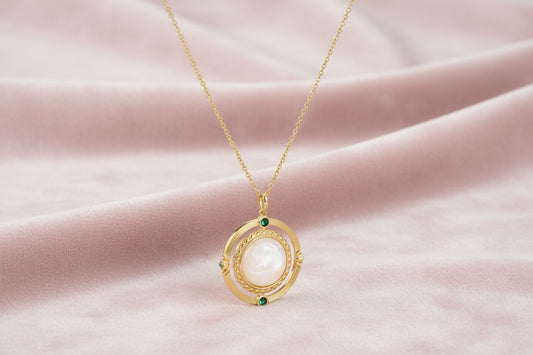 Gold pendant necklace with circular orbital design, iridescent mother-of-pearl center, and green zirconia accents
