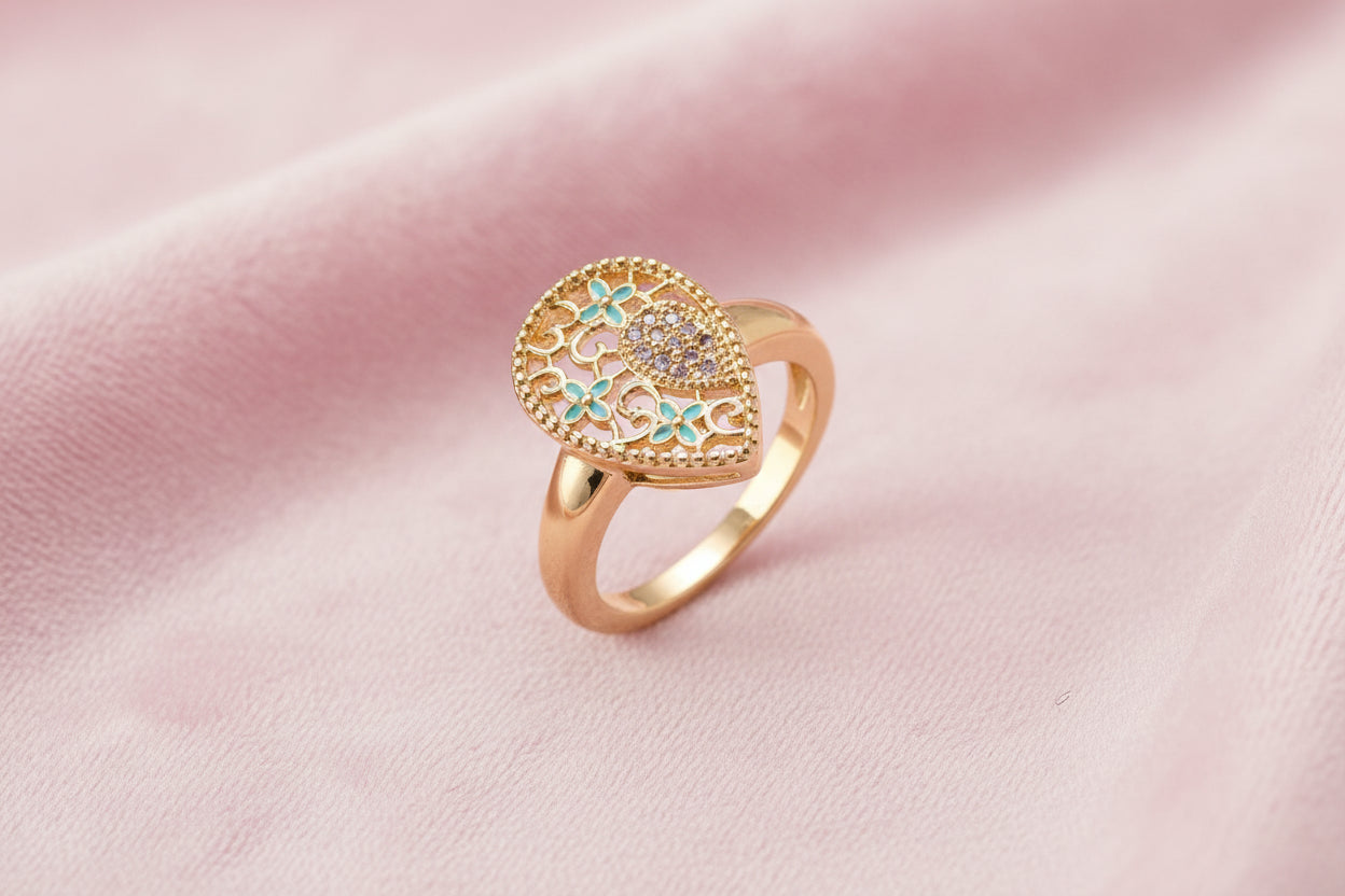 Teardrop-shaped gold-plated ring with turquoise enamel flowers and crystal pavé detail on cream background