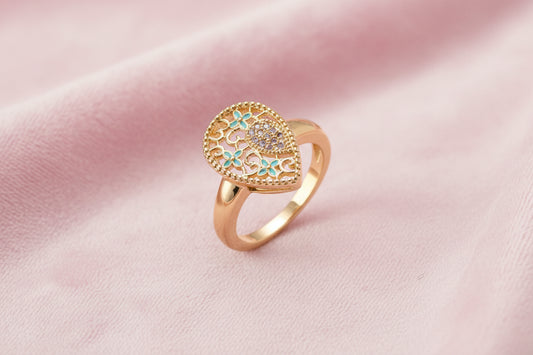 Teardrop-shaped gold-plated ring with turquoise enamel flowers and crystal pavé detail on cream background