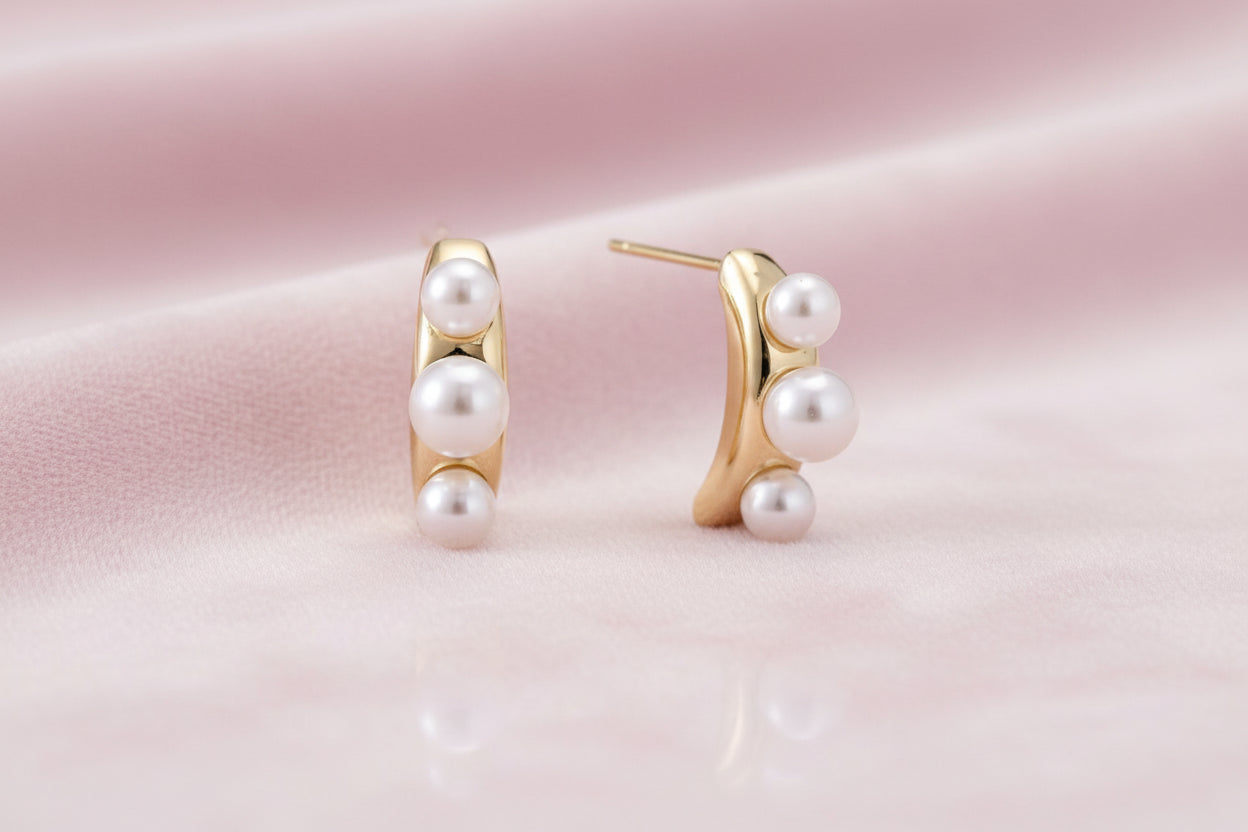 14K gold-plated curved stud earrings with three white freshwater pearls aligned vertically on cream background