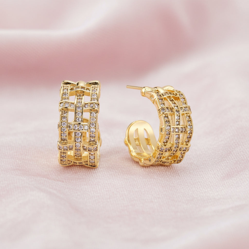 Gold-plated geometric hoop earrings with basket-weave lattice design and pavé crystal accents on cream background