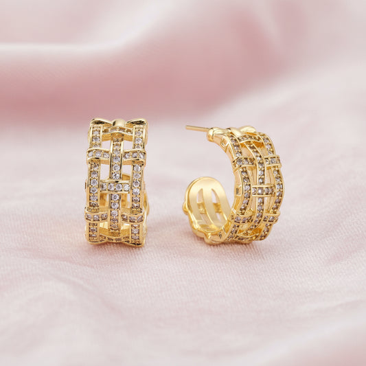 Gold-plated geometric hoop earrings with basket-weave lattice design and pavé crystal accents on cream background