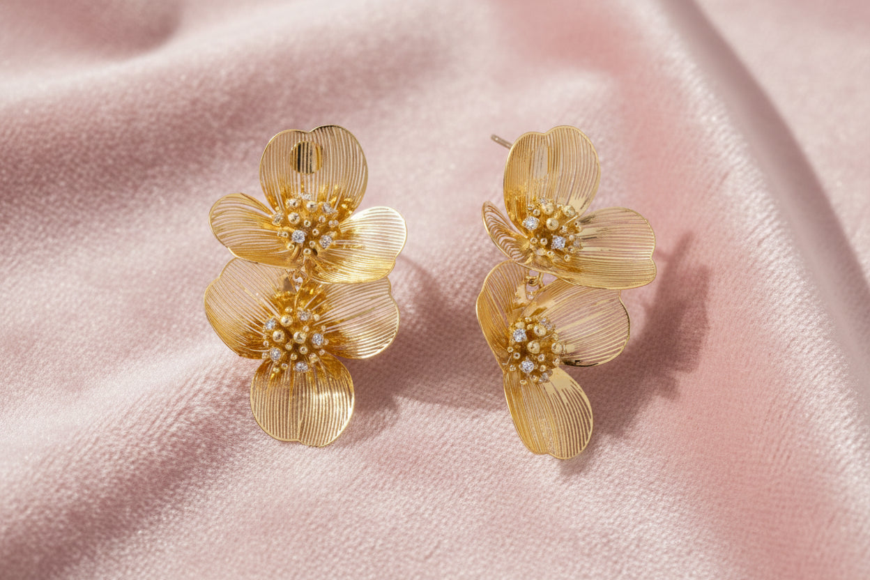 Pair of gold-plated double flower earrings with textured petals and crystal centers on cream background.