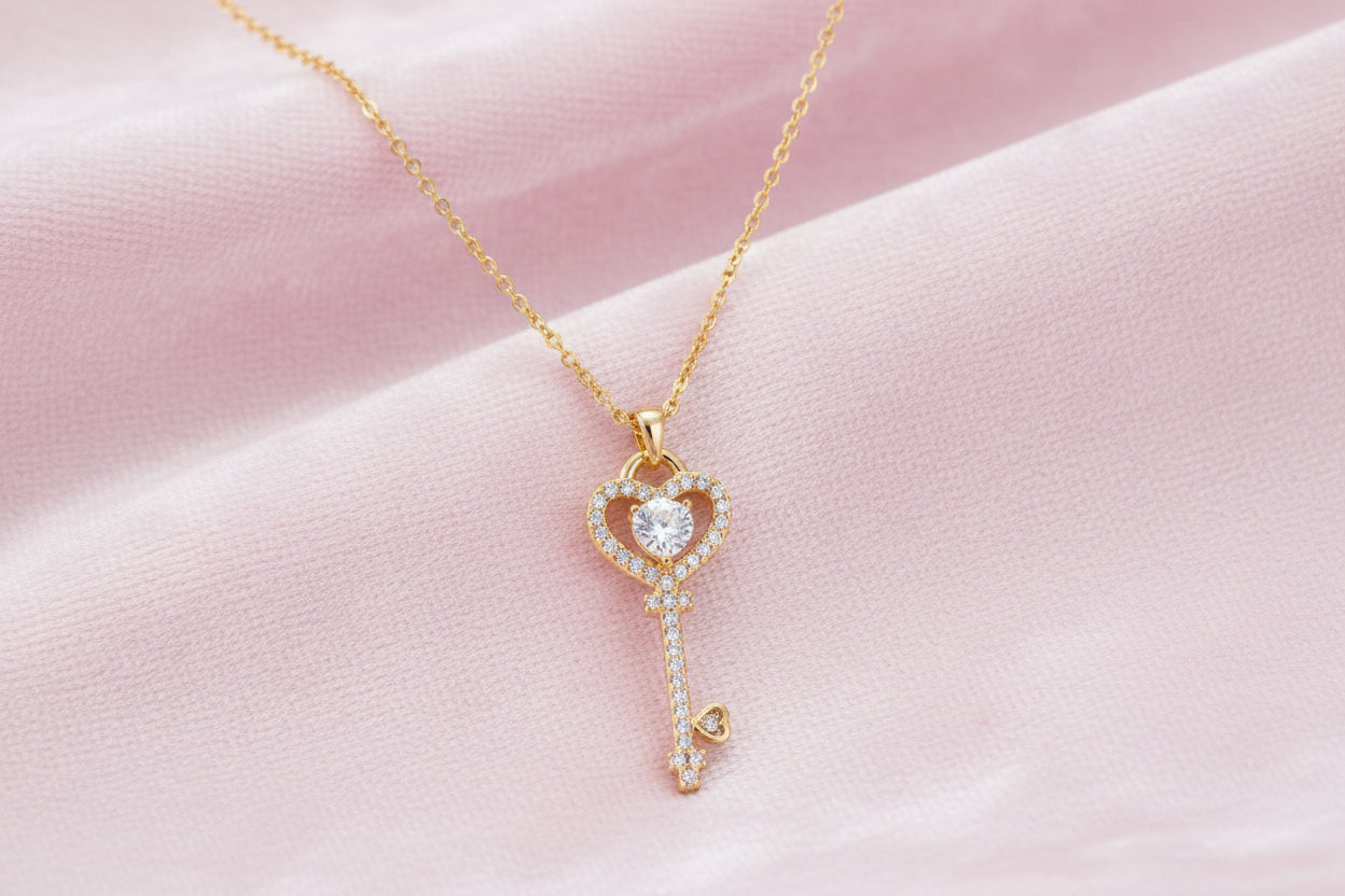 Delicate gold key pendant with heart-shaped bow and crystal pavé detailing on fine chain against cream background.