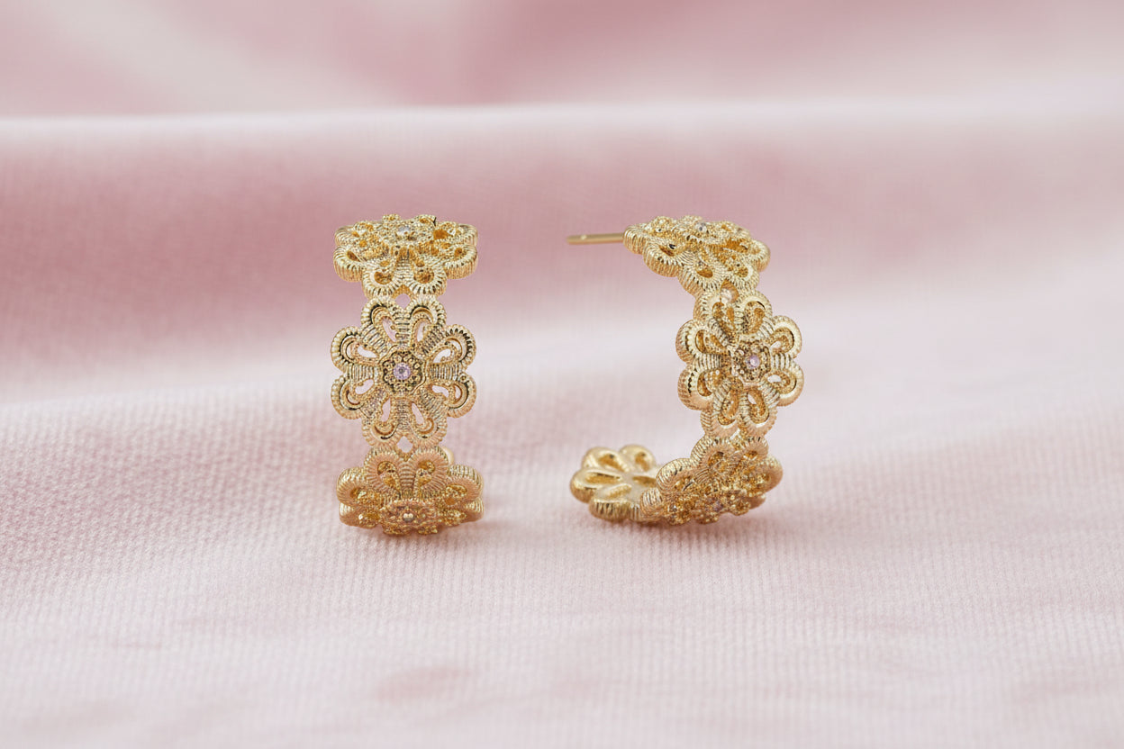 Gold hoop earrings with intricate three-dimensional floral filigree pattern in 14K gold plated brass on cream background