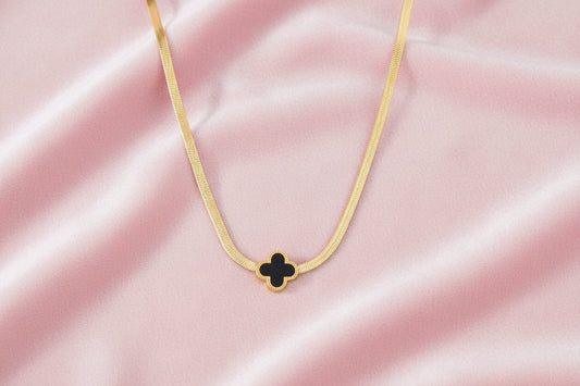 Dainty 18K gold-plated herringbone chain necklace with black enamel quatrefoil clover pendant on white background