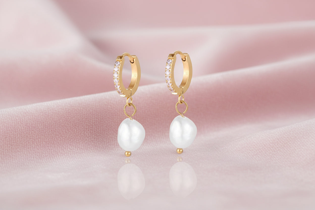 Gold huggie hoop earrings with pavé crystals and white freshwater pearl drops on cream background