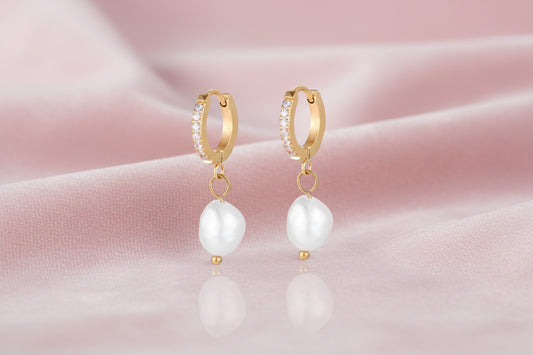 Gold huggie hoop earrings with pavé crystals and white freshwater pearl drops on cream background