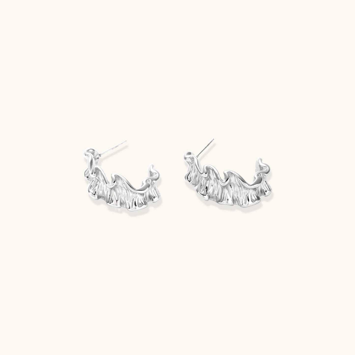 White gold plated sculptural hoop earrings with organic wavy edges and reflective metallic finish on cream background