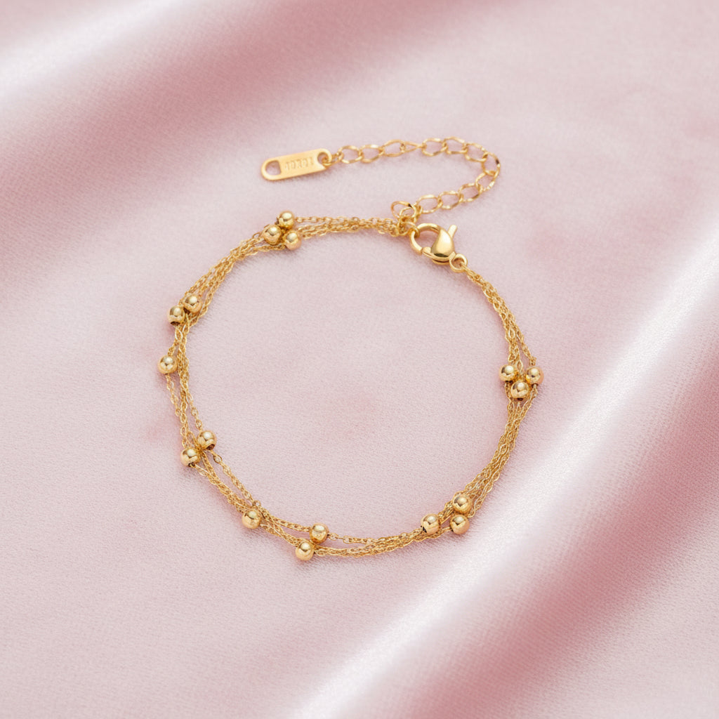 Three-strand gold-plated bracelet with clustered ball beads and adjustable clasp on cream background