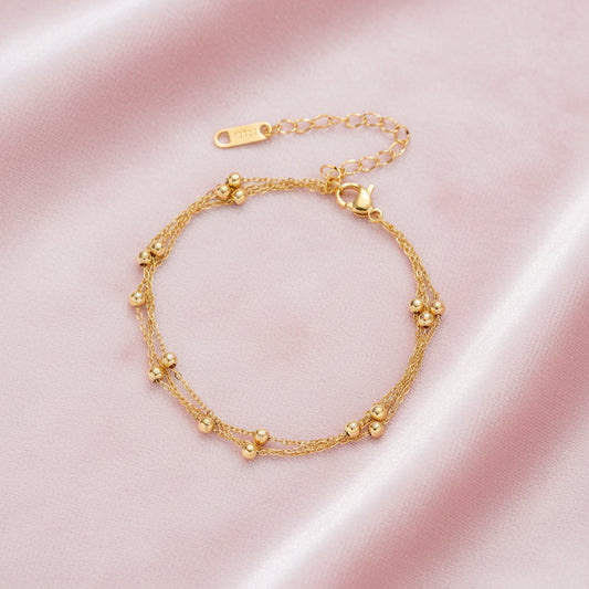 Three-strand gold-plated bracelet with clustered ball beads and adjustable clasp on cream background