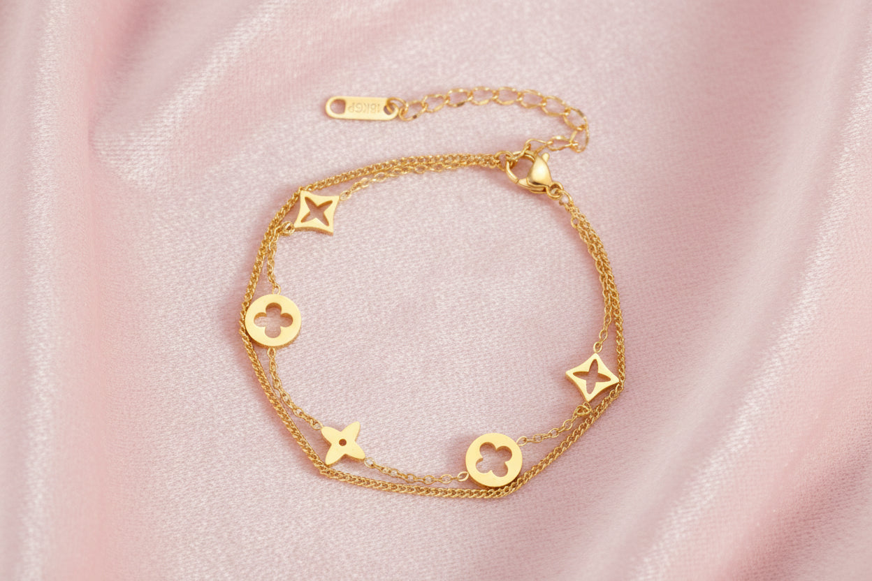Double-layer gold-plated bracelet with quatrefoil and star charms on cream background, 18K gold finish.