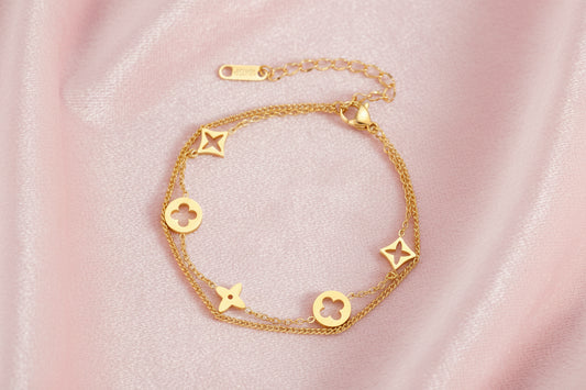 Double-layer gold-plated bracelet with quatrefoil and star charms on cream background, 18K gold finish.