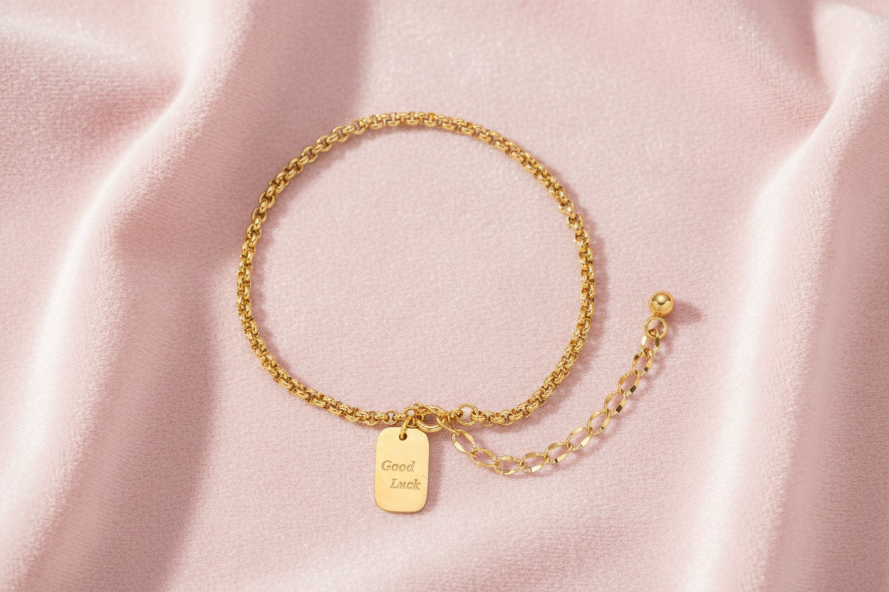 Delicate 18K gold-plated chain bracelet with Good Luck engraved rectangular pendant on cream background