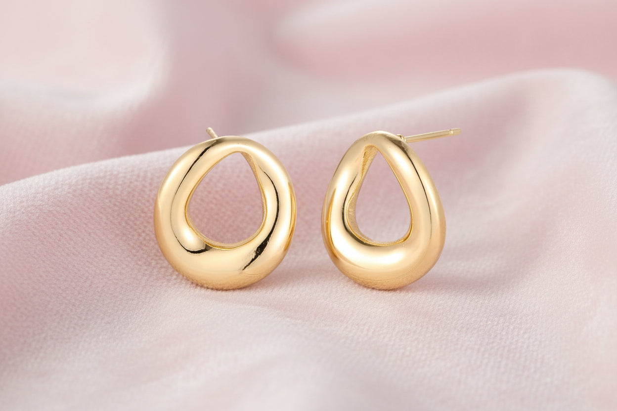 Pair of polished 18K gold-plated stainless steel teardrop earrings with hollow centers on cream background