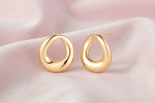 Pair of polished 18K gold-plated stainless steel teardrop earrings with hollow centers on cream background