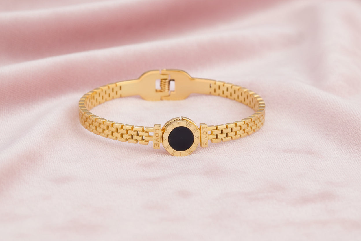 Gold mesh bracelet with circular black mother of pearl medallion featuring Roman numeral engravings and hinged clasp