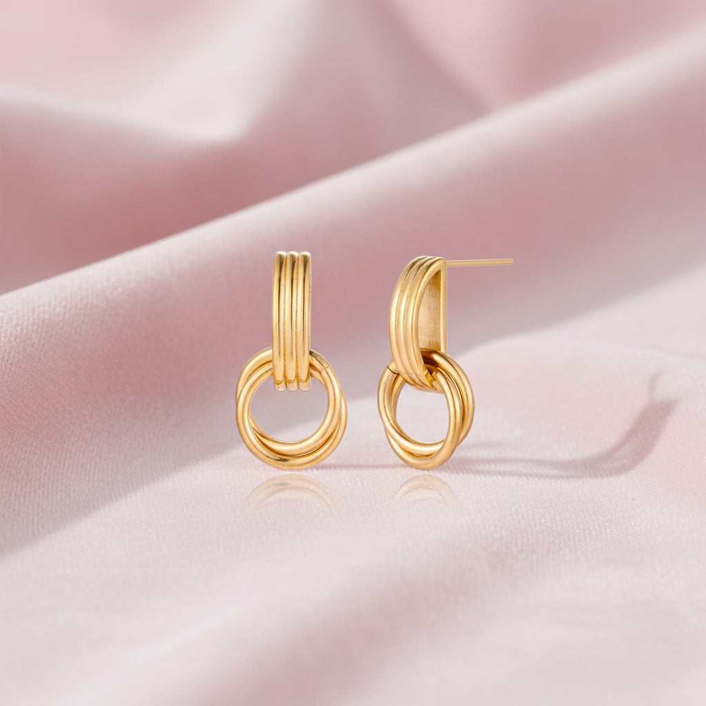 Gold stud earrings with vertical ridged bar connecting to triple interlocking circular rings on white background