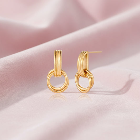 Gold stud earrings with vertical ridged bar connecting to triple interlocking circular rings on white background