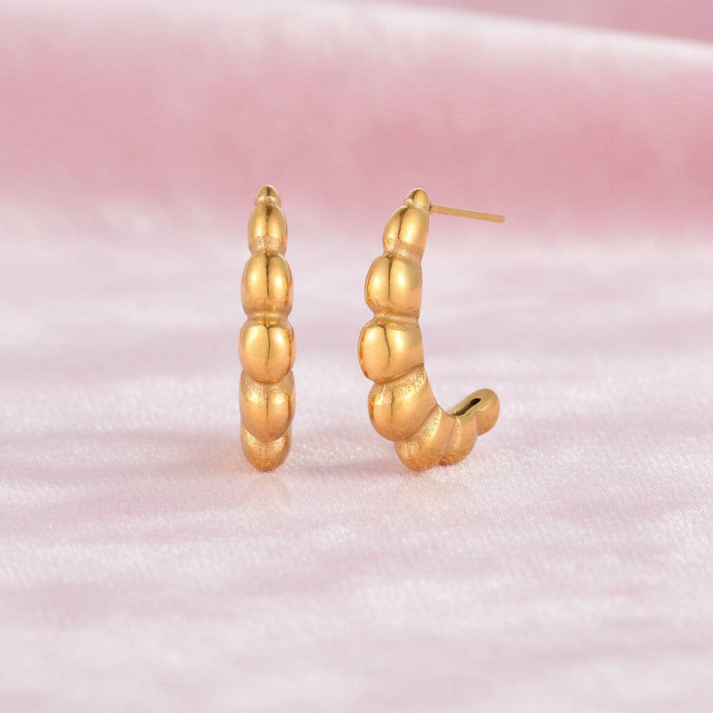 Gold-plated chunky hoop earrings with ridged bubble texture on cream background