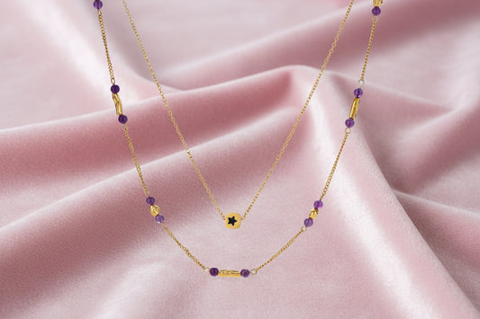Two layered gold-tone necklaces with purple stone beads and star pendant against cream background.