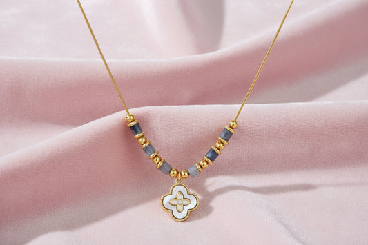 Gold-toned beaded necklace with grey stones and quatrefoil abalone shell pendant on cream background.
