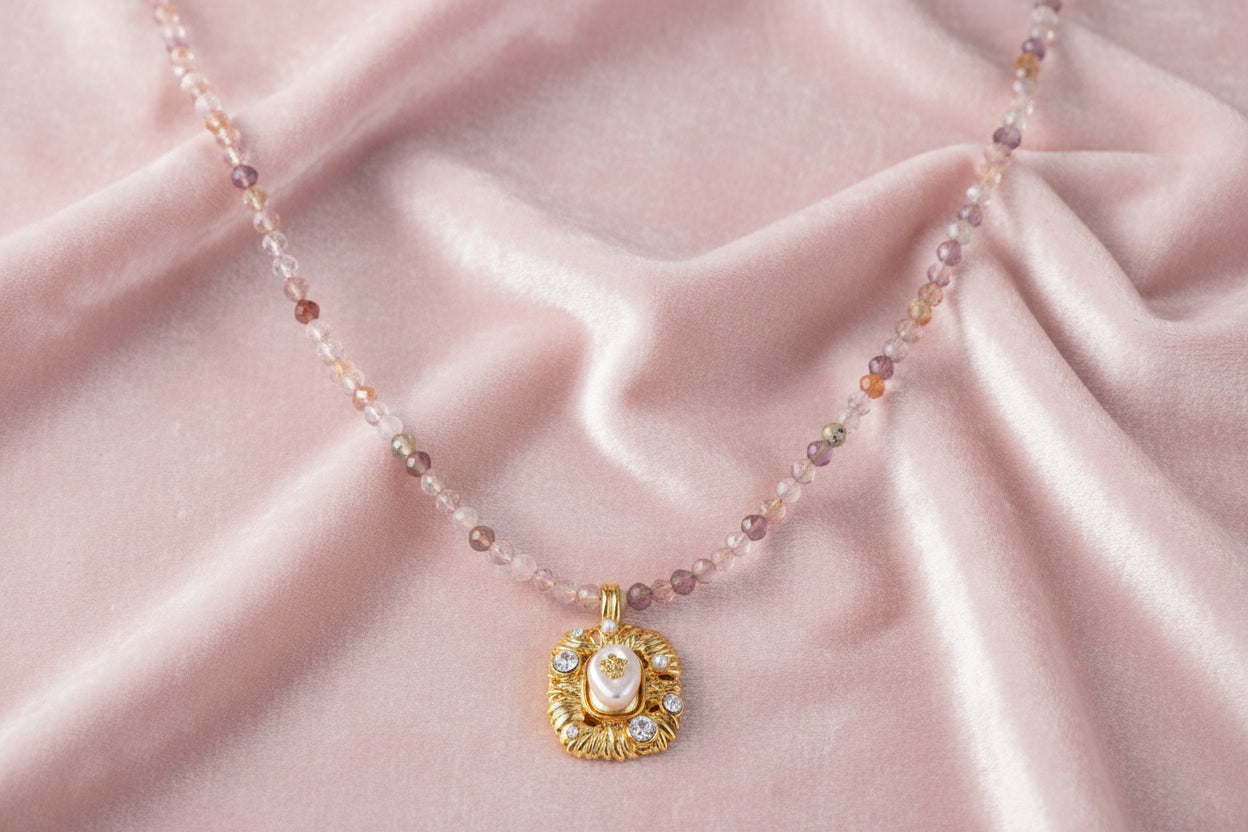 Ornate gold-plated pendant necklace with multicolored gemstone beads in purple, pink and clear tones on white background