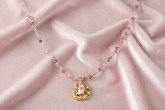 Ornate gold-plated pendant necklace with multicolored gemstone beads in purple, pink and clear tones on white background