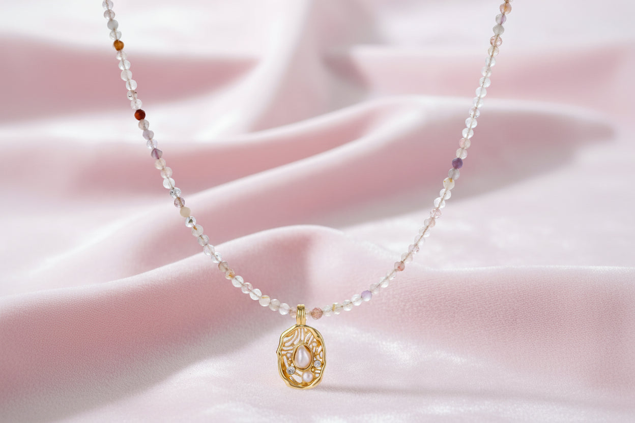 Delicate gold-plated necklace with mixed gemstone beads and ornate oval pendant on white background