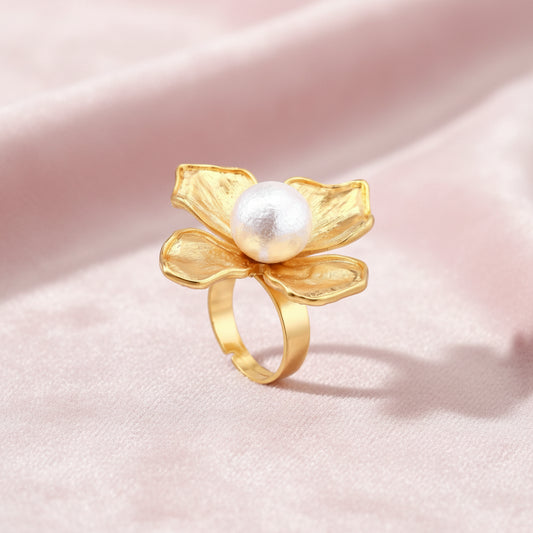 Gold-plated flower ring with textured petals and white cotton pearl center on cream background