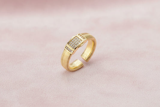 Gold-plated adjustable ring with ribbed band and rectangular pavé cubic zirconia panel on white background.