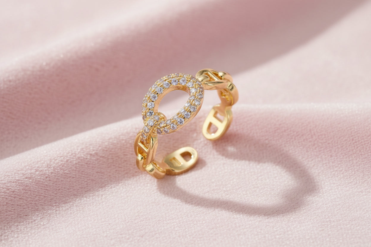 Gold-plated brass chain link ring with one oval CZ-pavé segment on cream background, adjustable cuff style.